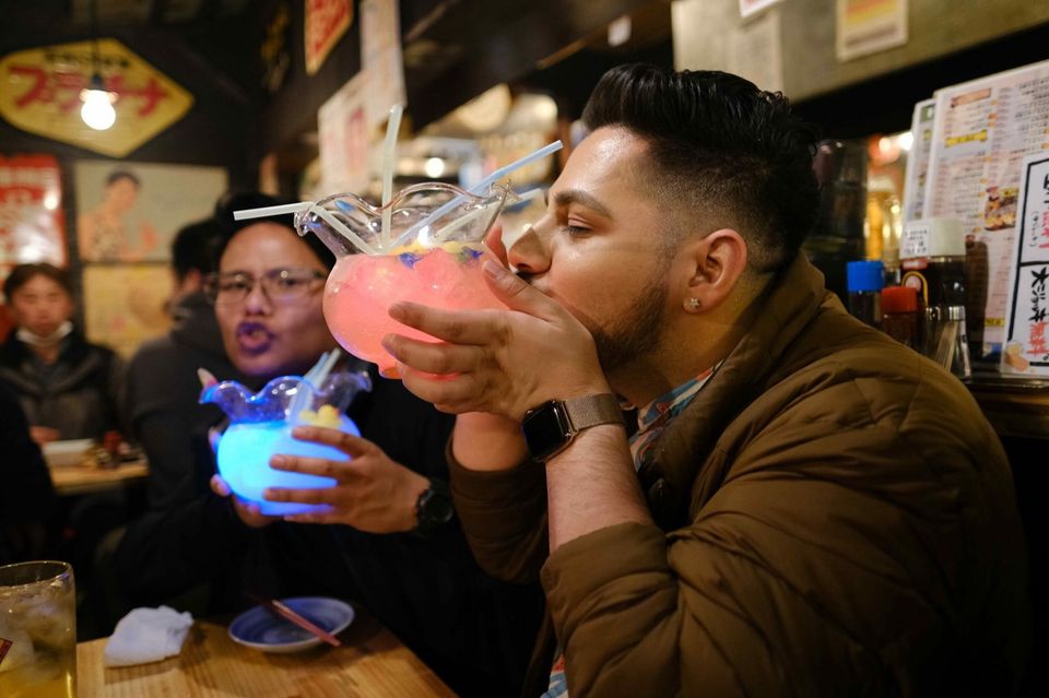 Two friends cheering with drinks at a bar in Tokyo