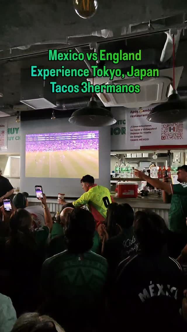 Fans in green jerseys watching a Mexico World Cup match on a big screen at a taco restaurant in Tokyo
