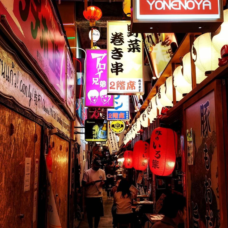 Paper lanterns glowing over a row of small izakaya at night