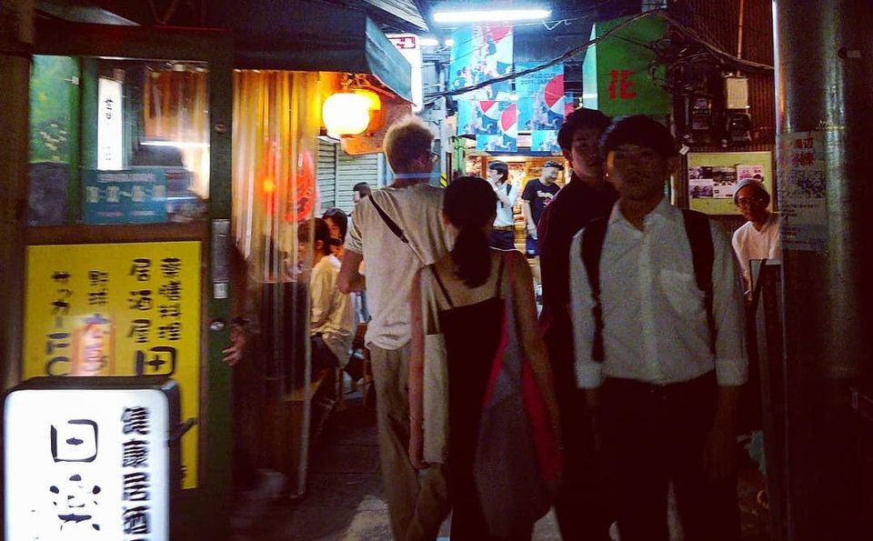Narrow yokocho alley at night with people walking past small bars